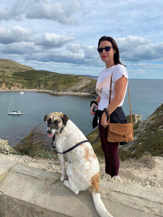 A woman standing by the coast with her dog, alongside a lit Ruth at Essence Paradise Beach candle and the text “Are candles safe for animals? Let’s have a chat…” promoting a new blog post.