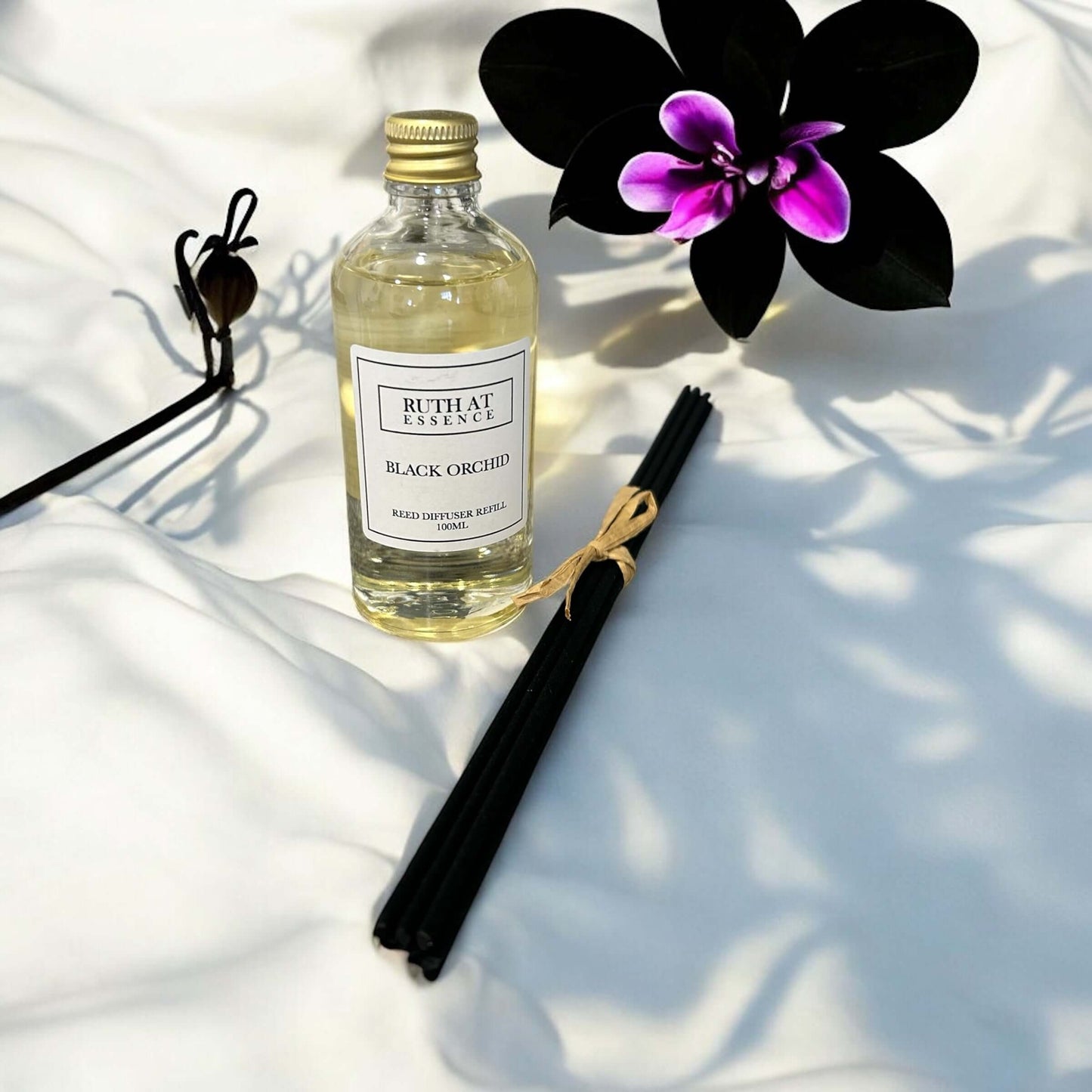 Black Orchid diffuser refill 100ml with new reeds on a soft surface, surrounded by an orchid flower.