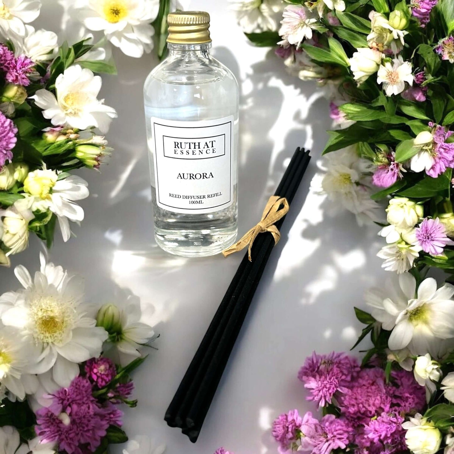 Aurora - Floral Diffuser Refill 100ml bottle surrounded by colorful flowers and diffuser sticks.
