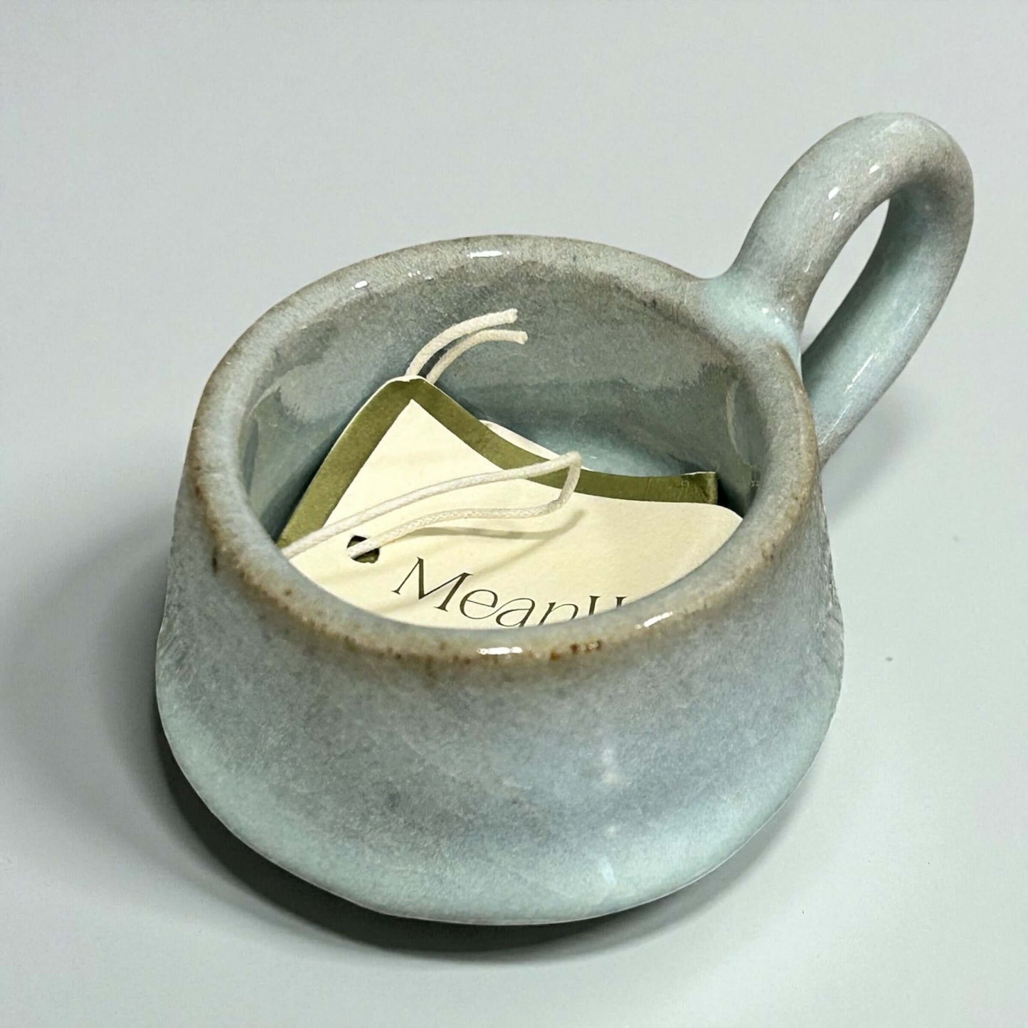 Stoneware Eggshell Tea-Light Holder with handle and tags inside, showcasing soft eggshell glaze and cozy design.