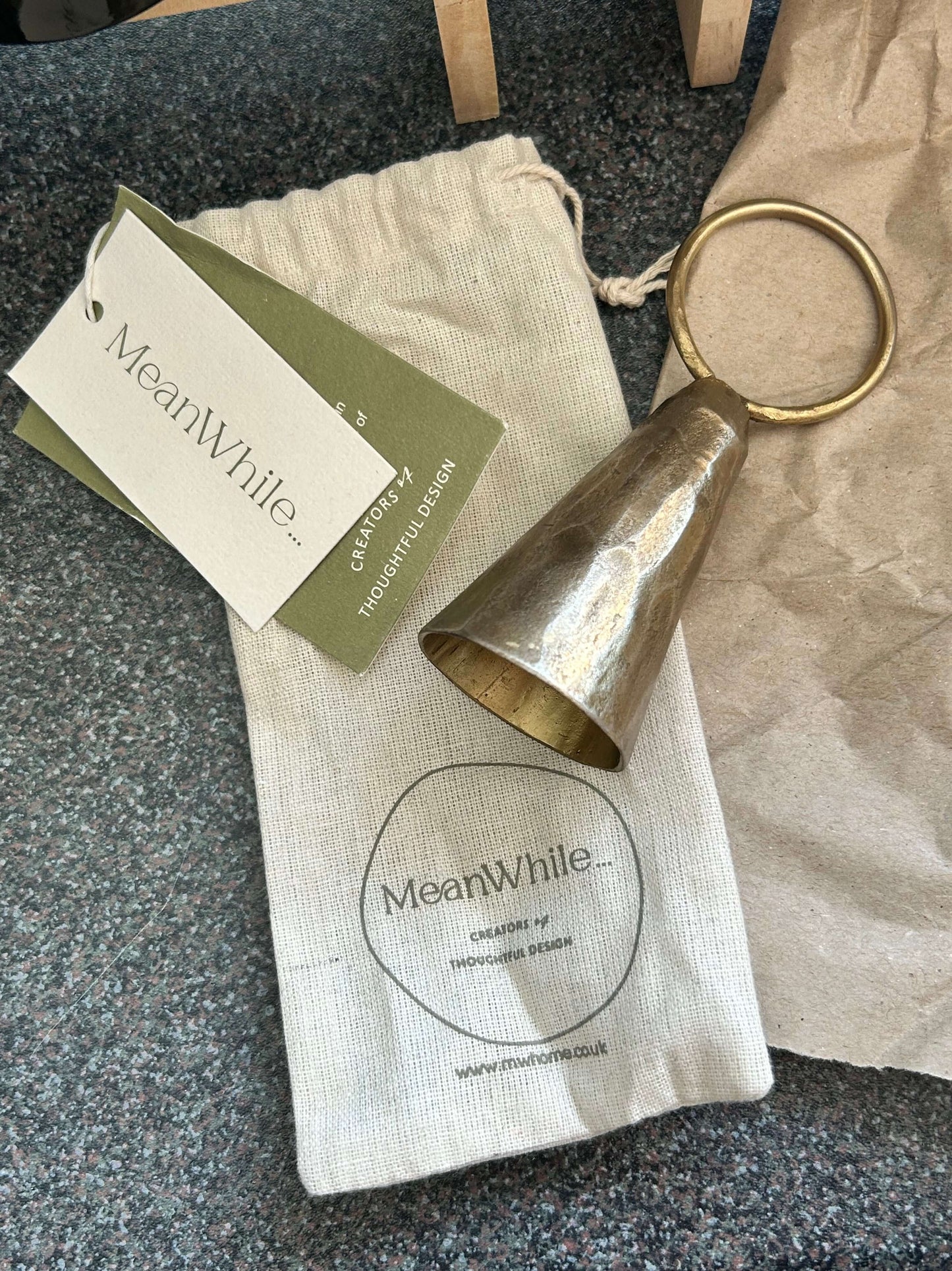 Handmade brass candle snuffer resting on cotton pouch with MeanWhile branding, showcasing ethical craftsmanship and recycled materials.