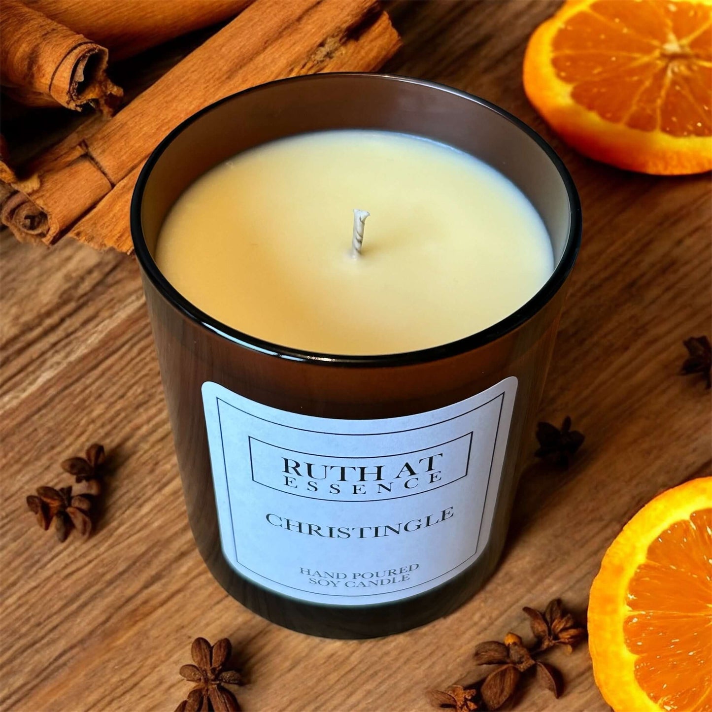 Christingle candle in a glass container surrounded by cinnamon sticks and orange slices, creating a festive holiday decor.