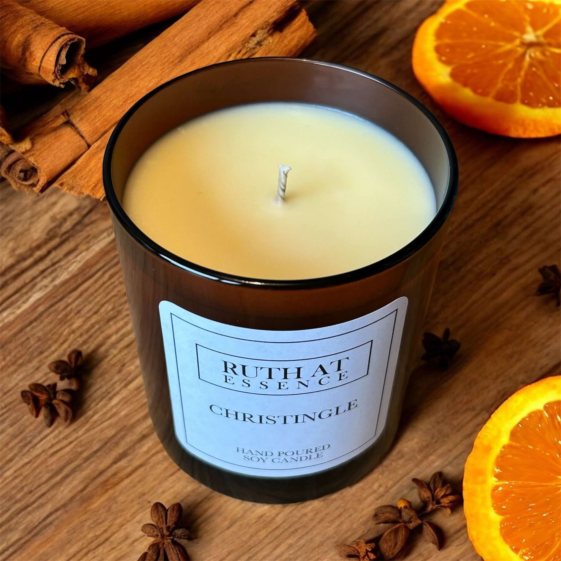 Christingle candle in a glass container surrounded by cinnamon sticks and orange slices, creating a festive holiday decor.