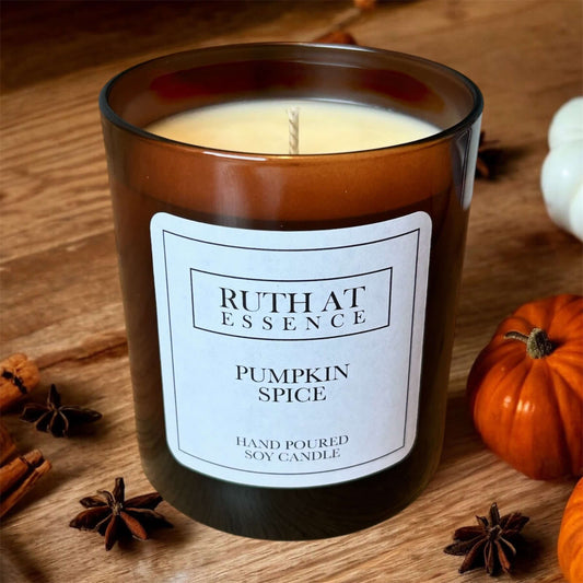 Pumpkin Spice Candle in amber glass jar surrounded by cinnamon and pumpkin decorations.