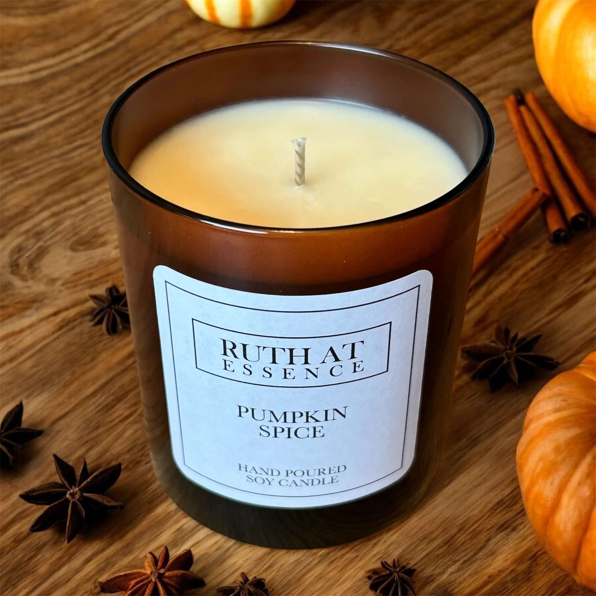 Pumpkin Spice Candle in decorative jar with label, surrounded by cinnamon and pumpkins, creating a warm festive atmosphere.