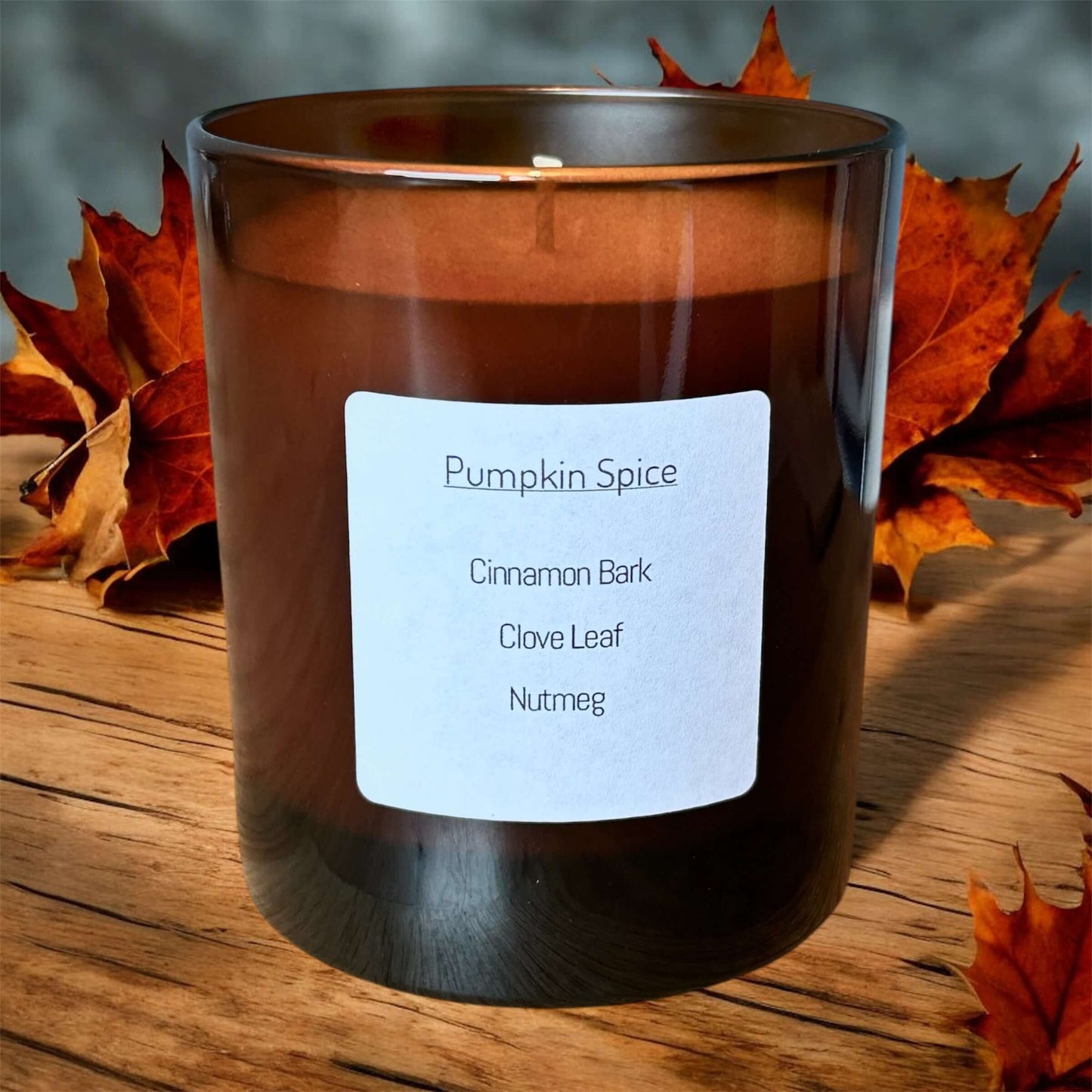 Pumpkin Spice Candle featuring cinnamon bark, clove leaf, and nutmeg, set against an autumn background.