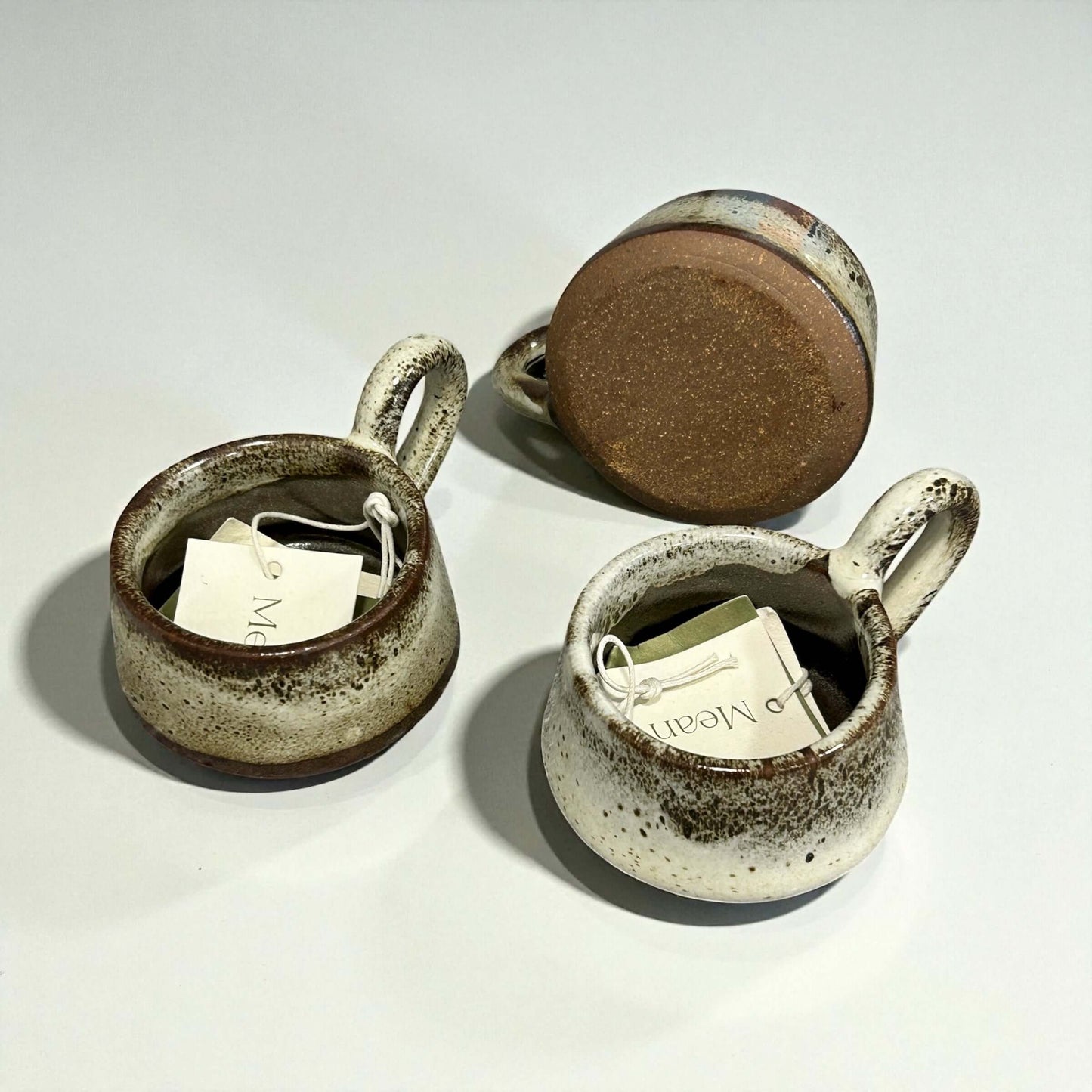 Three Stoneware Tawny Tea-Light Holders with tags, showcasing their unique textures and warm colors.