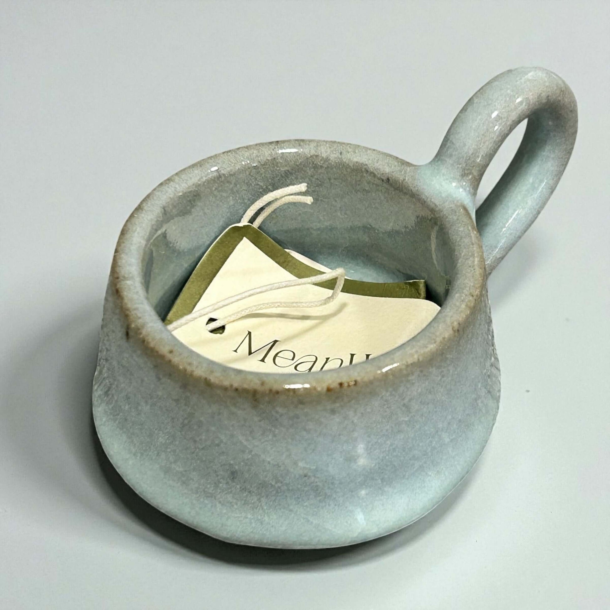 Stoneware Eggshell Tea-Light Holder with handle and tags inside, showcasing soft eggshell glaze and cozy design.